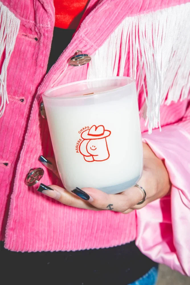 White coconut soy candle with saddle leather scent and red assless chaps cowboy hat design on the side