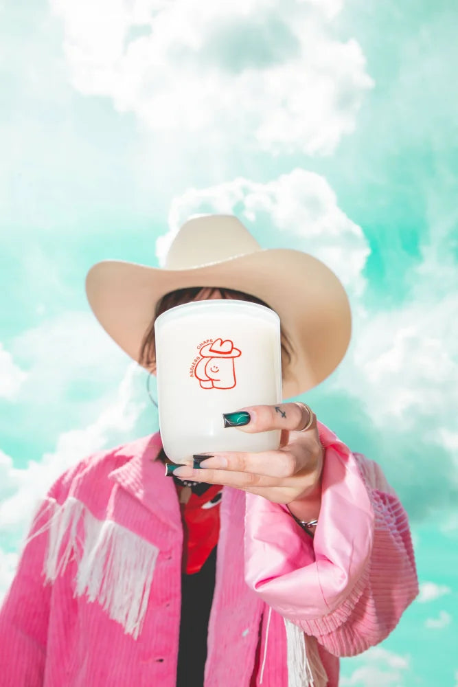 White ceramic candle with red cartoon cowboy hat design in 8oz saddle leather coconut soy candle called assless chaps
