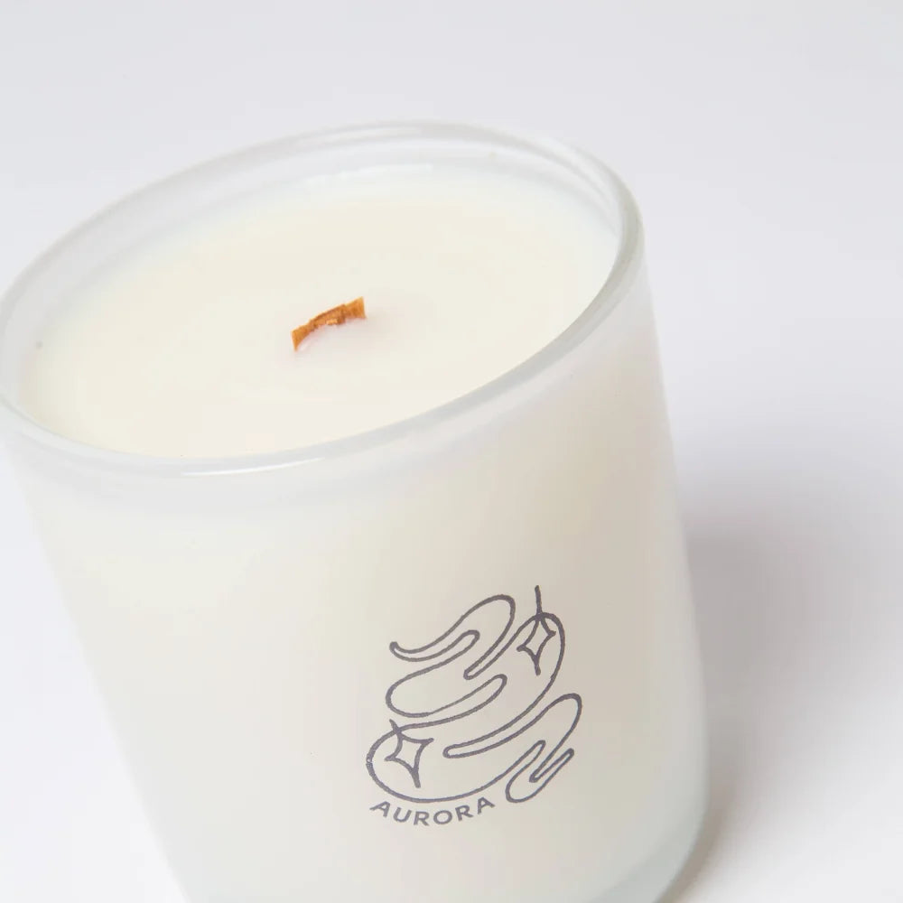 A white glass aurora candle with orange wooden wick and black logo made from coconut soy wax in mahogany teakwood scent