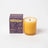 A golden amber glass coconut soy candle with wooden wick and milkjar logo beside a purple before sunrise box