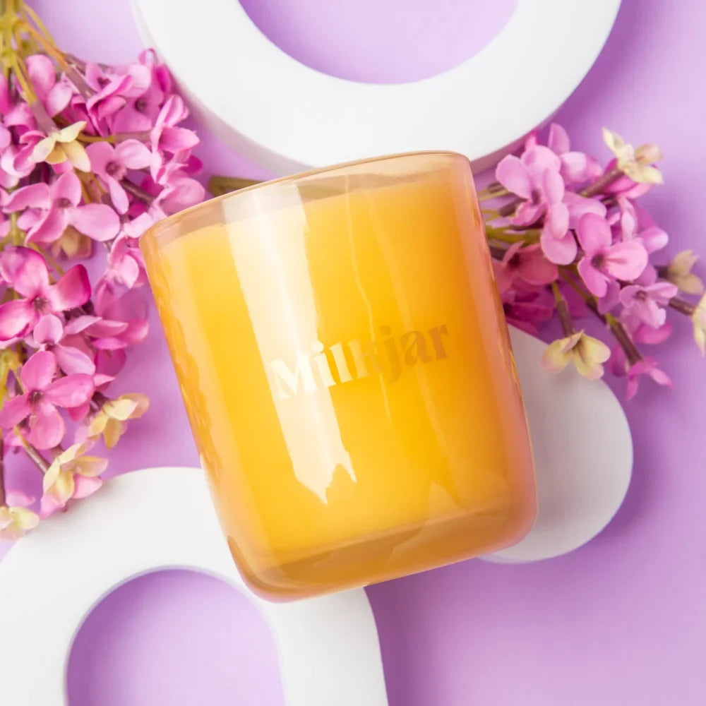 A translucent amber glass coconut soy candle jar by milkjar with pink flowers perfect for angus oliver rugs decor