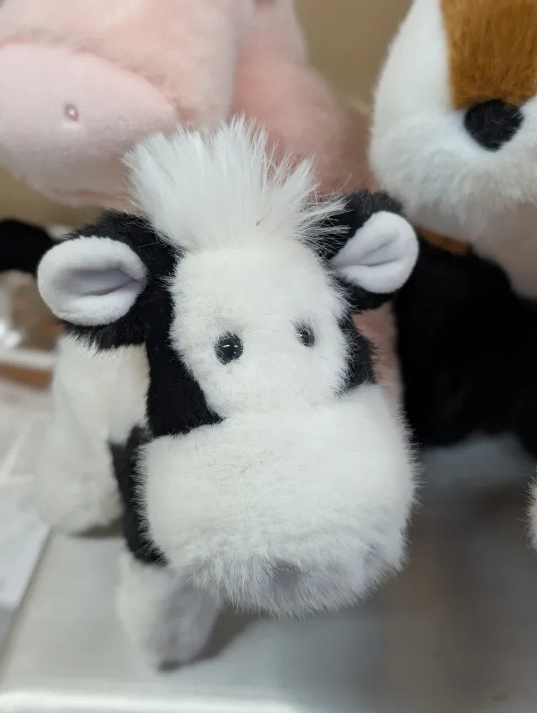 A plush black and white cow toy with fluffy fur soft ears and a rounded snout perfect for kids and decor