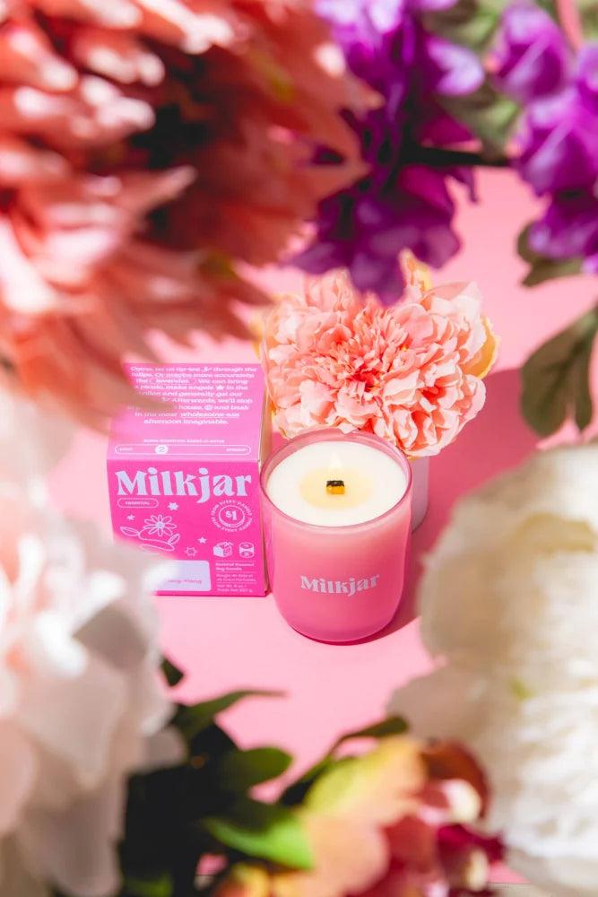A pink milkjar essential oil coconut soy candle with white wax and gold wick by angus oliver among pastel flowers