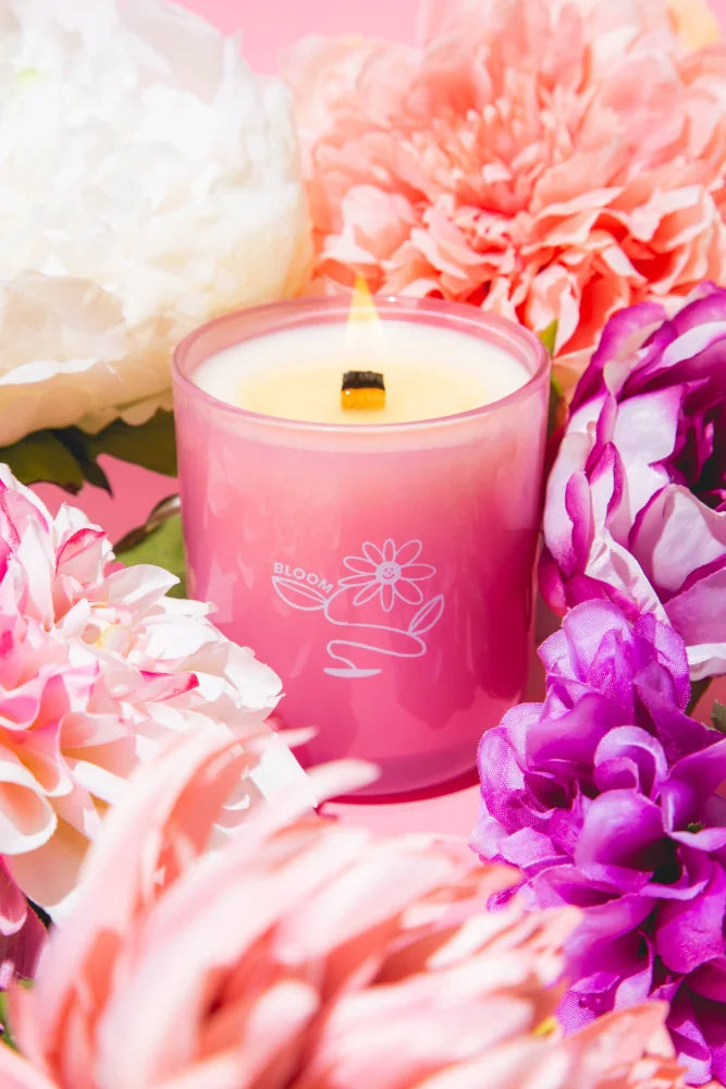 A pink glass bloom essential oil coconut soy candle with a lit wick and delicate white floral design by angus oliver