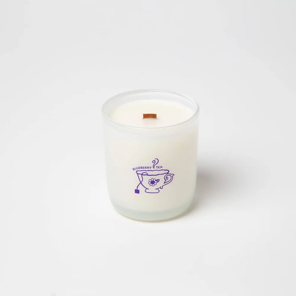 A white blueberry tea scented coconut soy wax candle with wooden wick in a frosted jar with a purple tea cup design