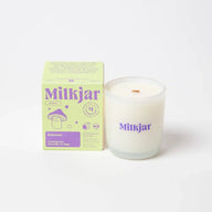 A white bohemia scented candle in a clear glass jar with purple branding and wooden wick made of coconut soy wax