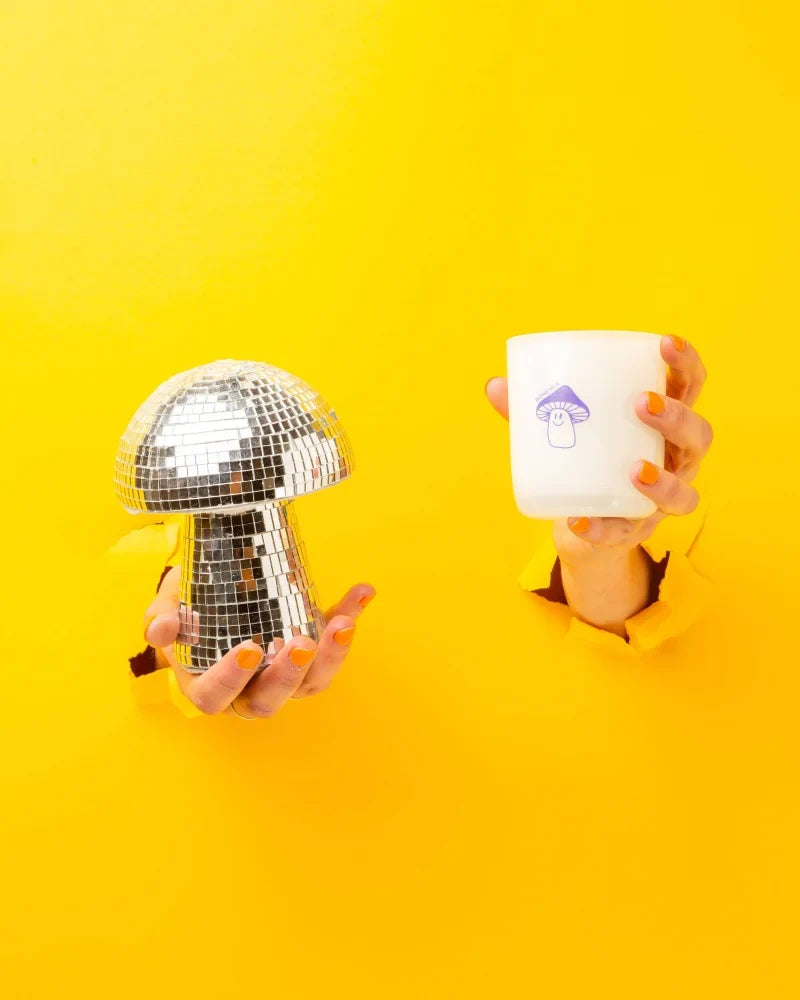 A silver disco ball mushroom ornament next to a bohemia coconut soy wax candle with lemongrass lavender sage scents