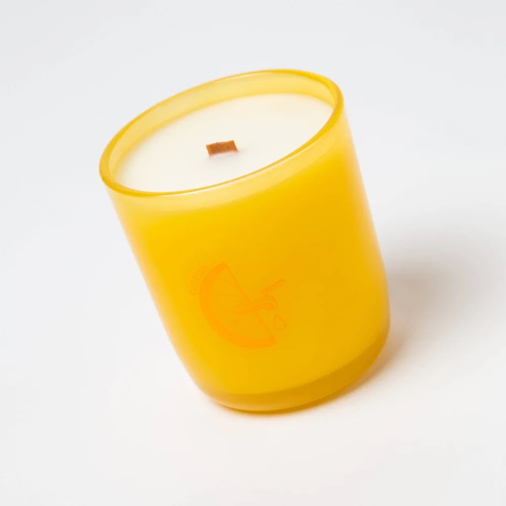A vibrant yellow citrus essential oil candle in frosted glass with white coconut soy wax and wooden wick