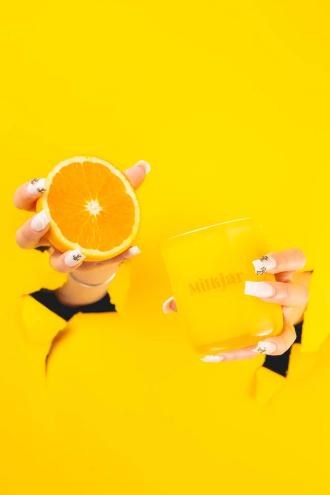 A vibrant yellow glass mug printed with milk held against yellow background next to citrus essential oil coconut soy candle