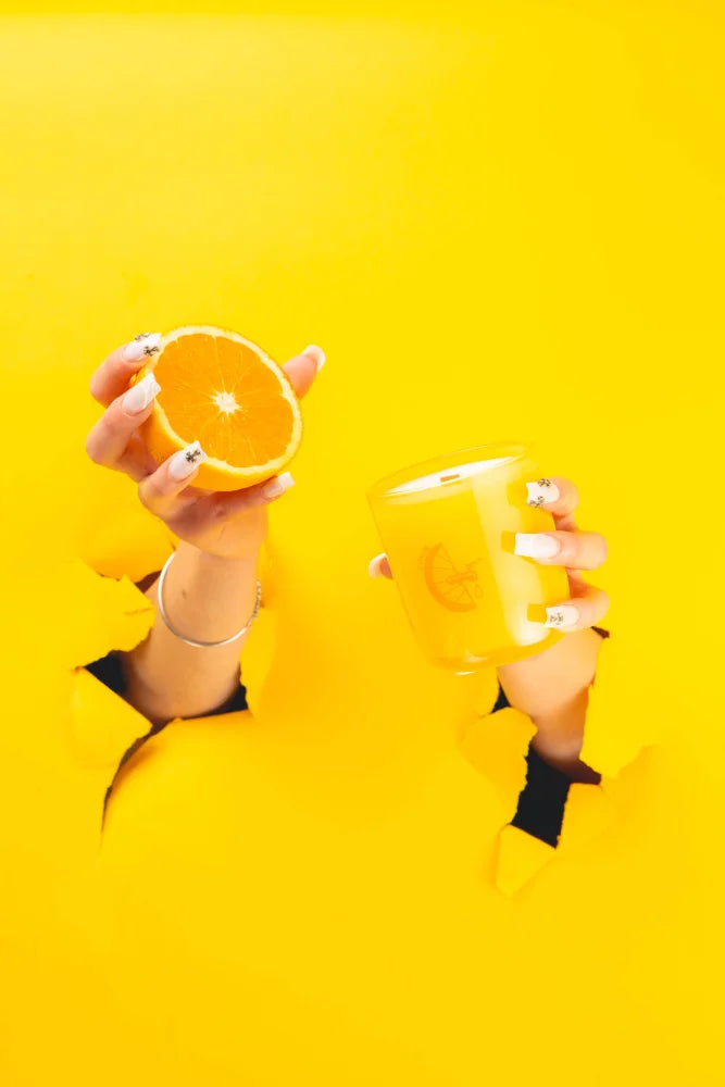 Hands hold half an orange and a yellow mug against a vibrant backdrop for citrus essential oil coconut soy candle