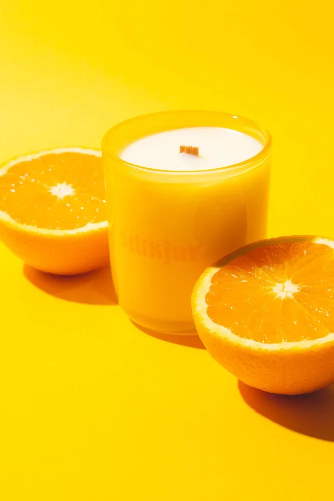 Vibrant orange citrus essential oil candle in coconut soy 8oz jar with wooden wick surrounded by halved oranges