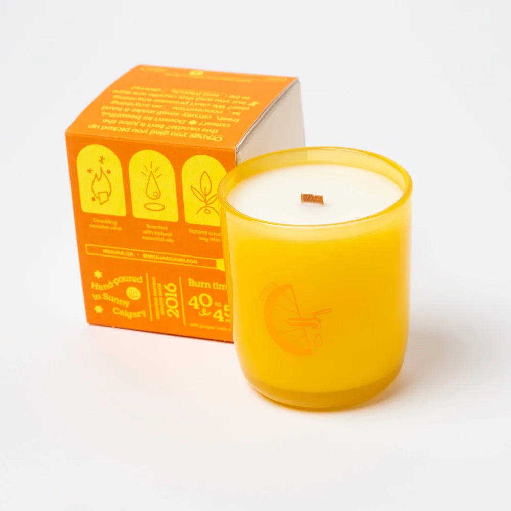 Vibrant yellow glass candle with wooden wick and embossed orange design made with essential oil coconut soy blend