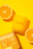 A vibrant orange citrus essential oil coconut soy candle in a clear glass jar with halved oranges on yellow background