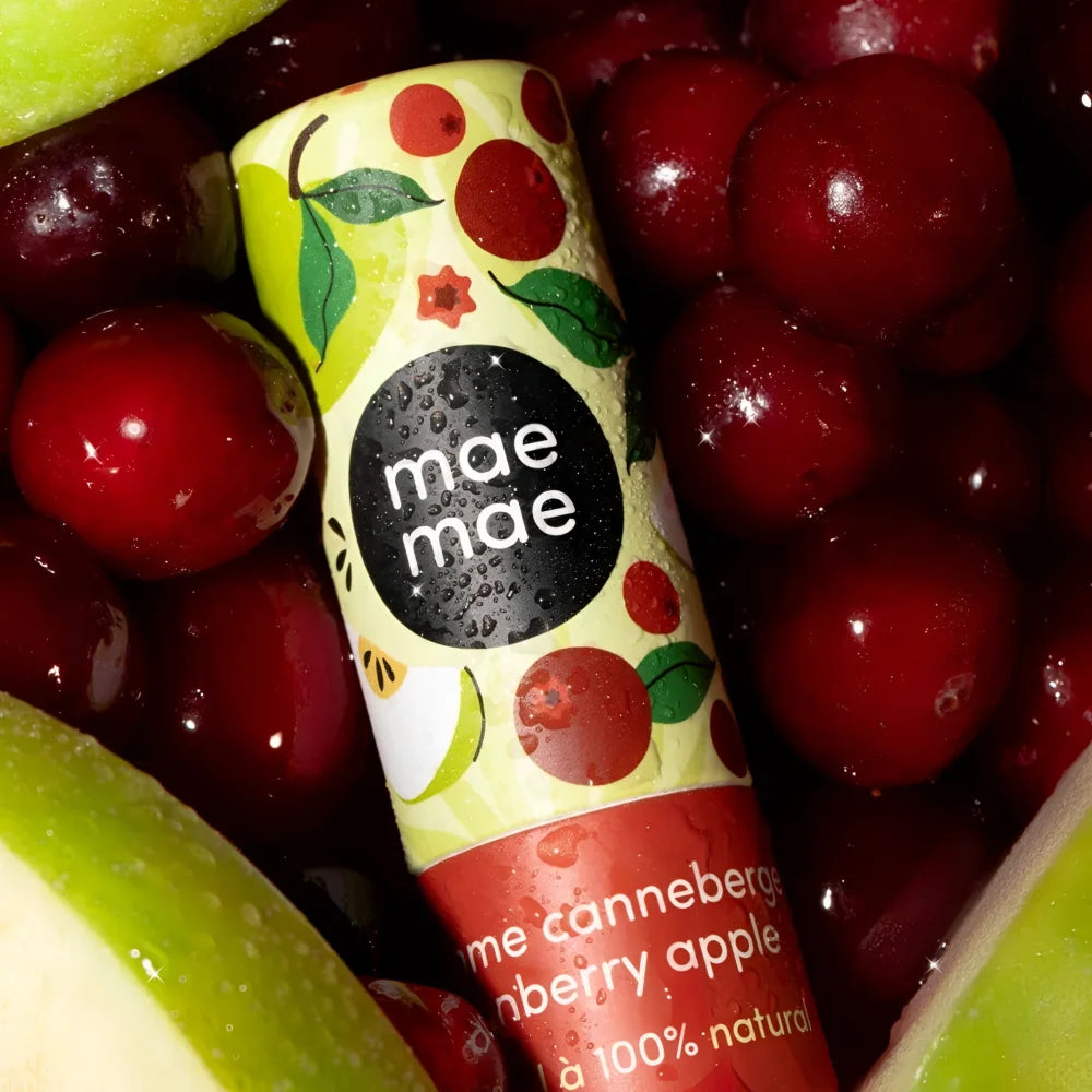 A cylindrical tube of mae mae cranberry apple natural lip balm with a bright yellow and red label with fruit illustrations