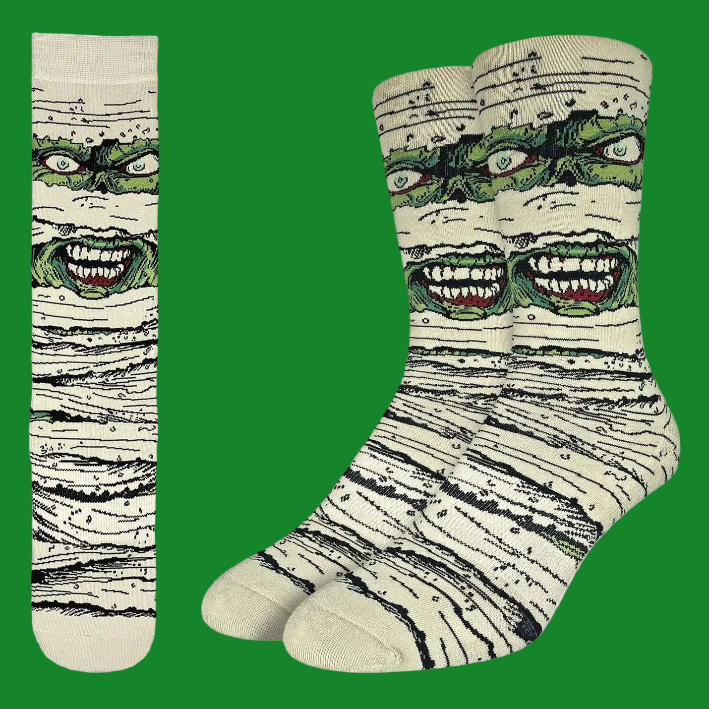 A pair of crew socks and a matching single sock shown flat against a white background. The socks feature a graphic print of a green monster face peeking through beige and black textured bandages, resembling a mummy.