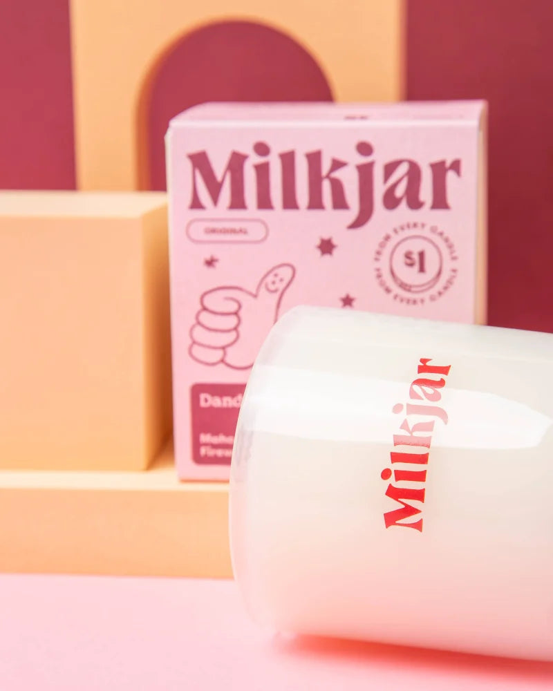 A translucent white milkjar glass candle with red lettering featuring coconut soy blend by angus oliver
