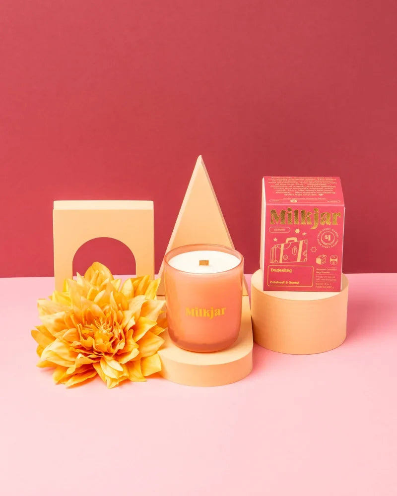A peach-colored glass jar candle with white coconut soy wax and gold milkjar logo darjeeling patchouli santal scent