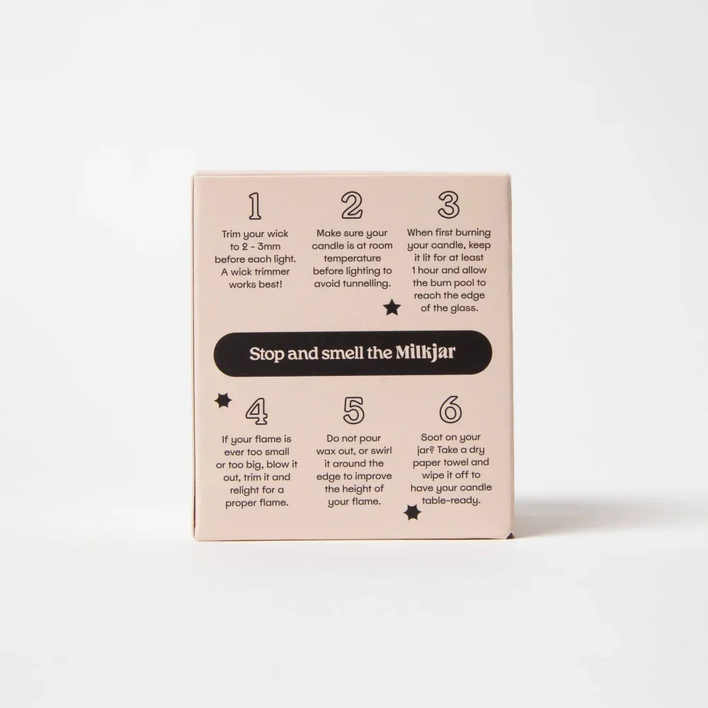 Back of a pale pink rectangular box showing six candle care steps for darjeeling patchouli santal coconut soy candle