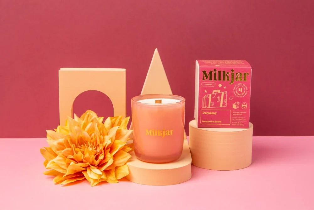 A peach-colored darjeeling patchouli santal coconut soy candle in a clear jar with gold lettering and wooden wick