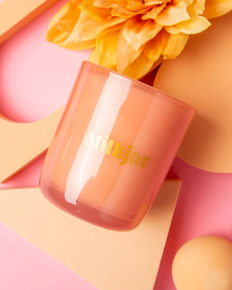 A translucent peach glass candle jar with gold mikjar lettering darjeeling patchouli and santal coconut soy candle