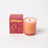 A peach-colored darjeeling patchouli and santal coconut soy candle in a frosted glass jar with wooden wick and gold lettering