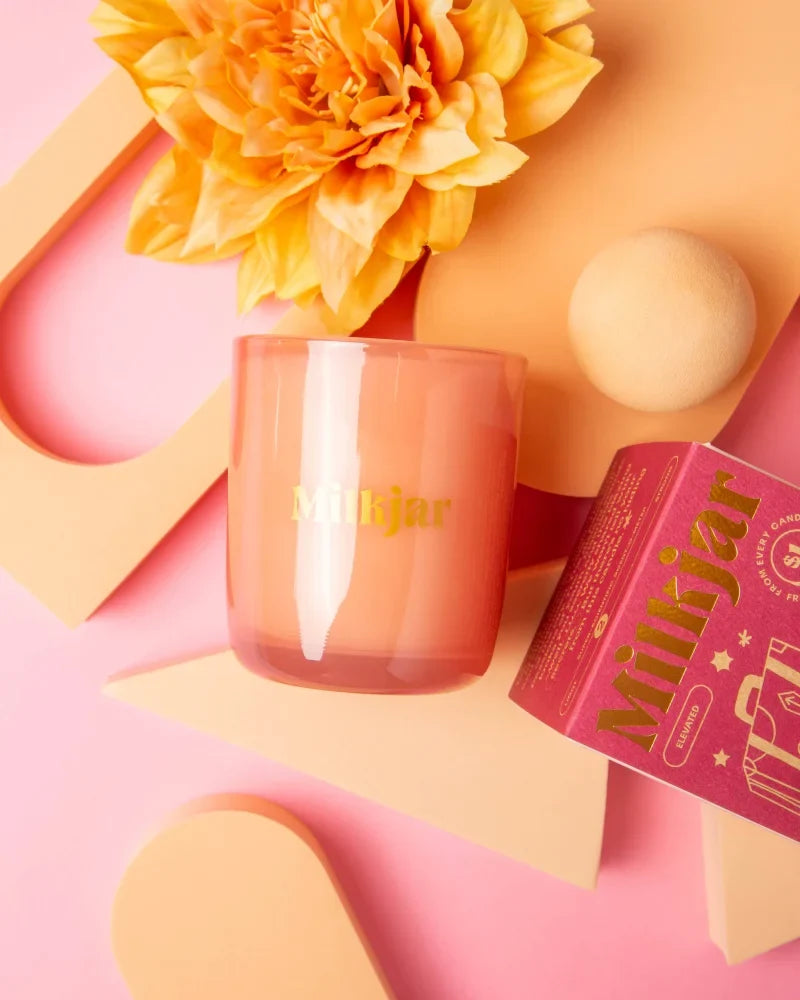 A peach-colored darjeeling patchouli santal coconut soy candle in a clear glass jar with gold lettering