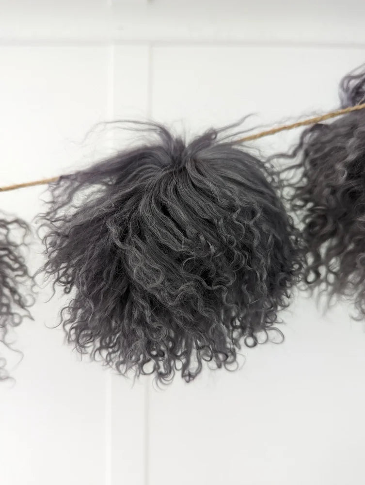 Dark grey sheepskin pom pom with curly black yarn on wooden stick