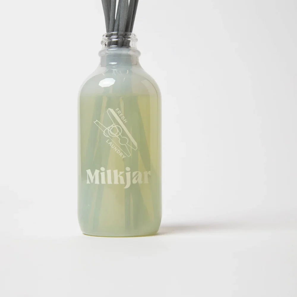 A translucent green glass milkjar reed diffuser with frosted finish labeled fresh laundry featuring rain cotton and french vanilla scent by angus oliver