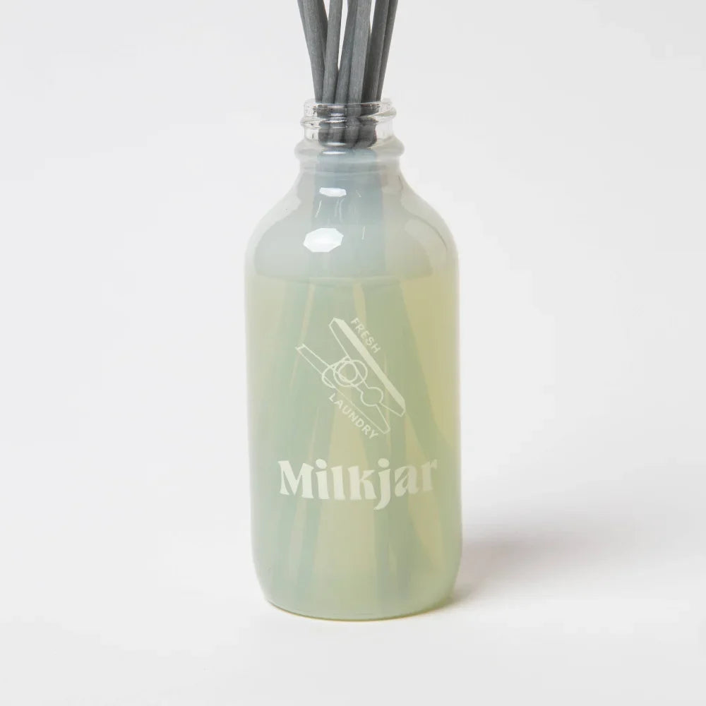 Translucent green glass reed diffuser bottle with dark gray sticks fresh laundry scent featuring french vanilla by angus oliver