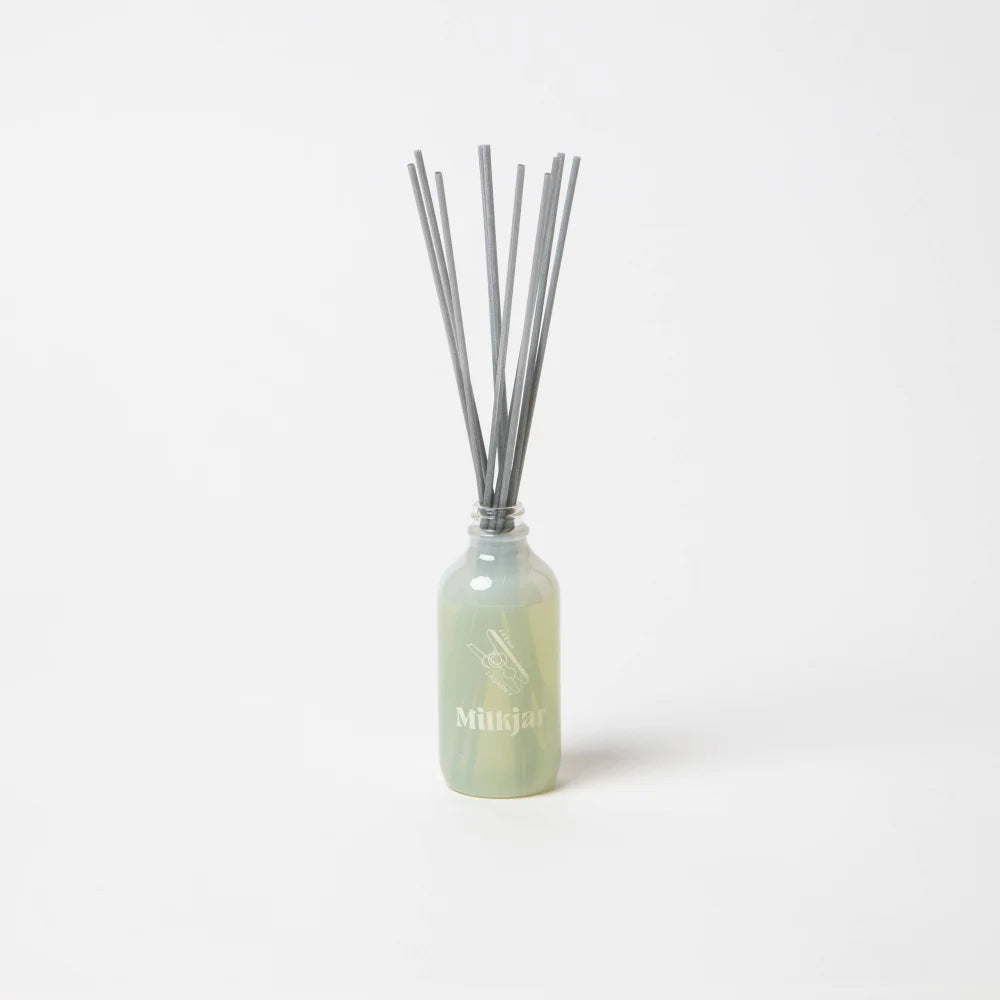 A sleek translucent green glass reed diffuser bottle with silver reeds for fresh laundry scent by angus oliver