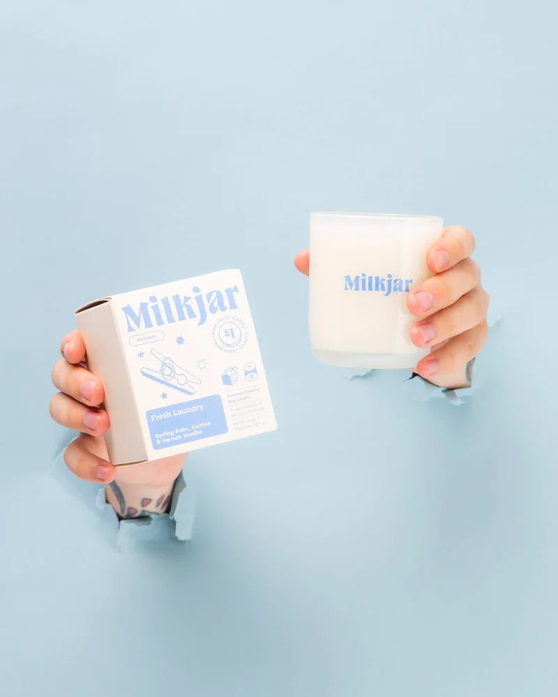 White milkjar candle in frosted glass with blue branding fresh laundry scent featuring french vanilla by angus oliver