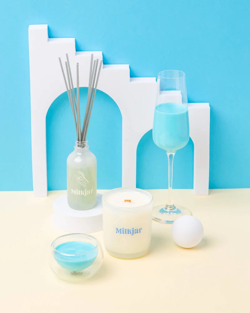 White cylindrical soy candle with blue milkjar branding fresh laundry scent featuring french vanilla by angus oliver