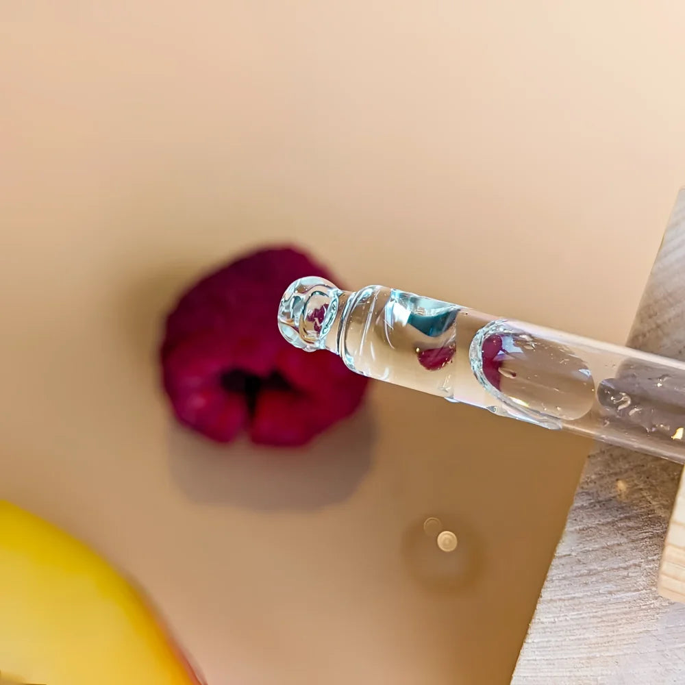 Clear glass dropper filled with glow & firm oil serum containing transparent seed oil and red flower petals