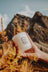 A white frosted glass golden hour candle with black hourglass drawing held against golden pine and mountains made from coconut soy wax