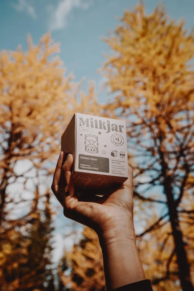 A white milkjar box for golden hour cashmere cedarwood coconut soy wax candle with sandglass illustration