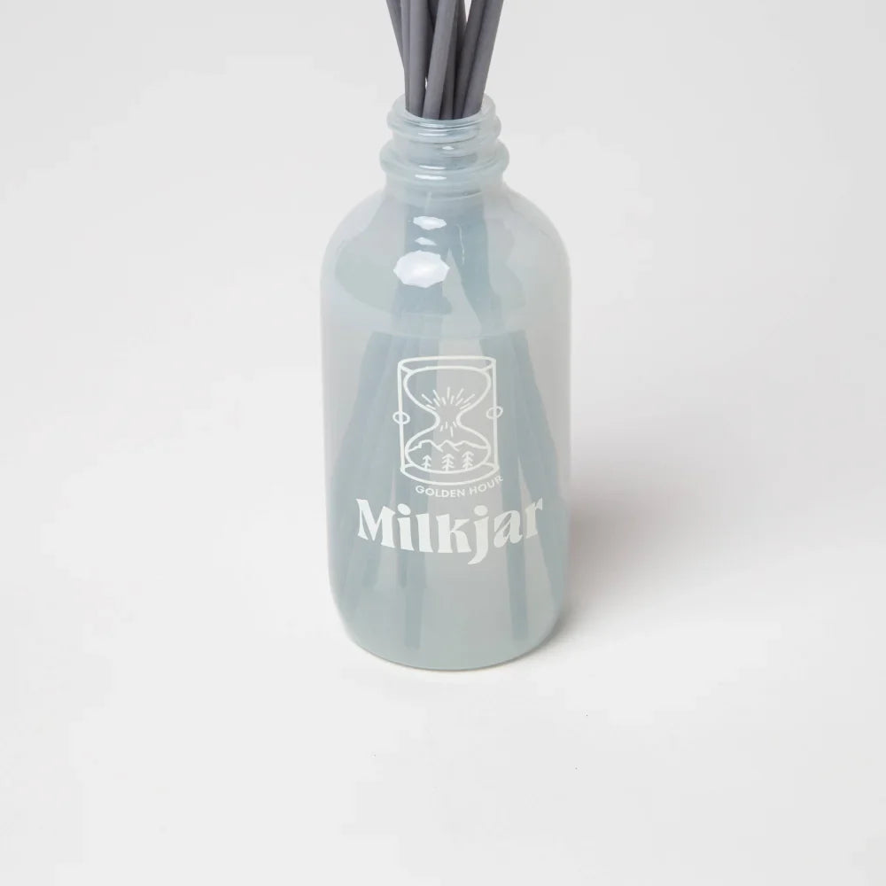 A translucent light gray glass reed diffuser bottle with white milkjar logo for golden hour scent blend