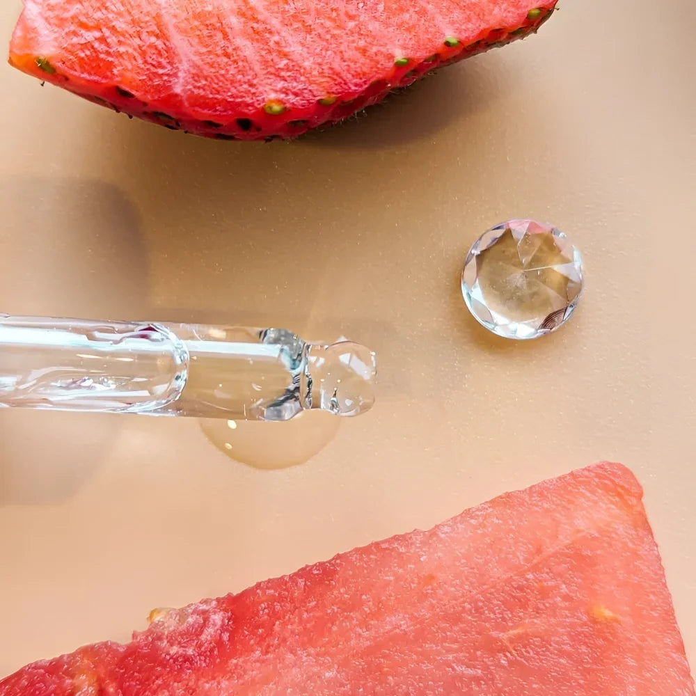 Clear glass dropper with a bulbous tip holding a drop of hydrate and purify oil serum with strawberry seed oil