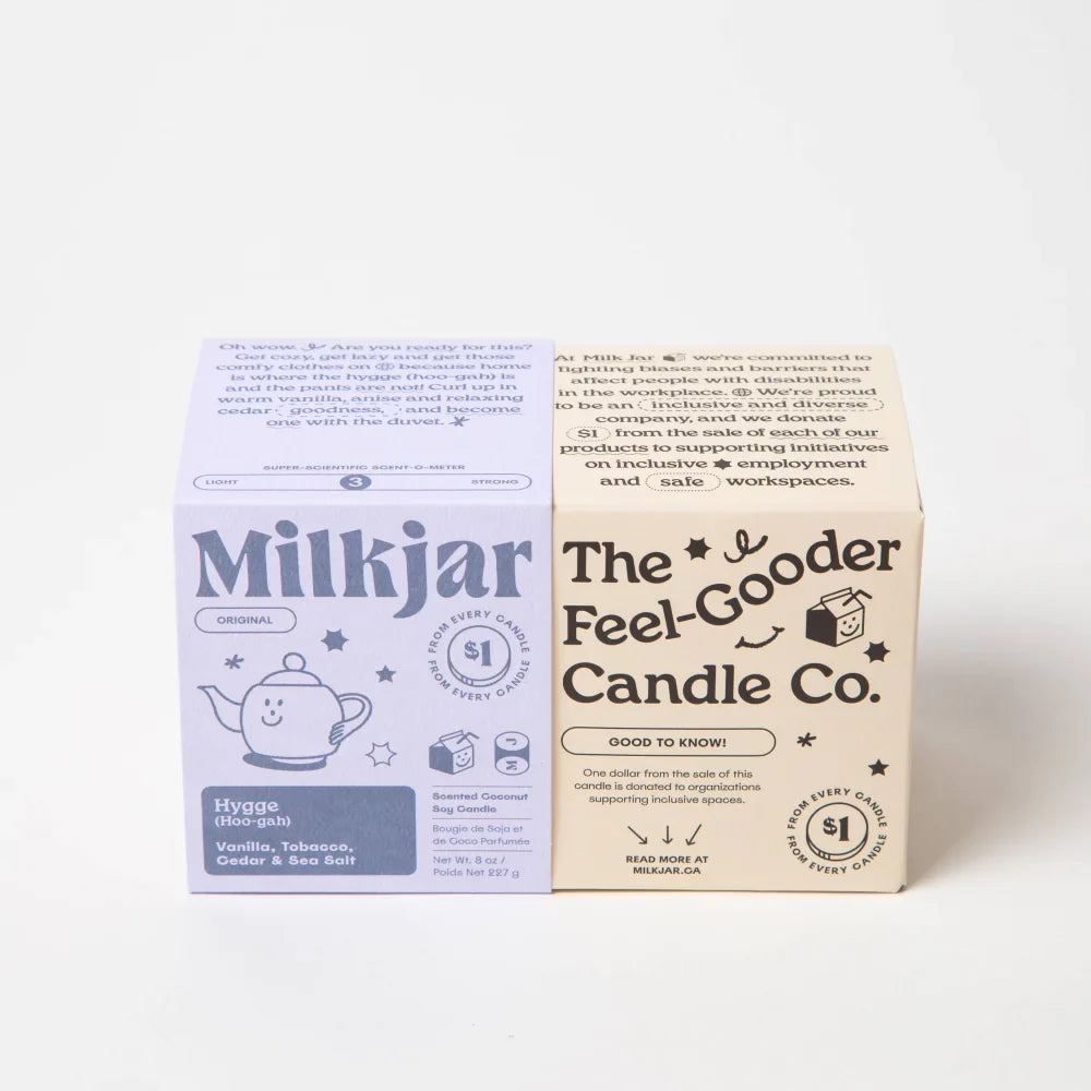 Lavender-colored milkjar coconut soy candle labeled hygge scent with vanilla tobacco cedar and sea salt and a smiling teapot illustration