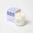 A creamy white coconut soy candle in a clear glass jar with a smiling teapot branded as hygge vanilla tobacco cedar