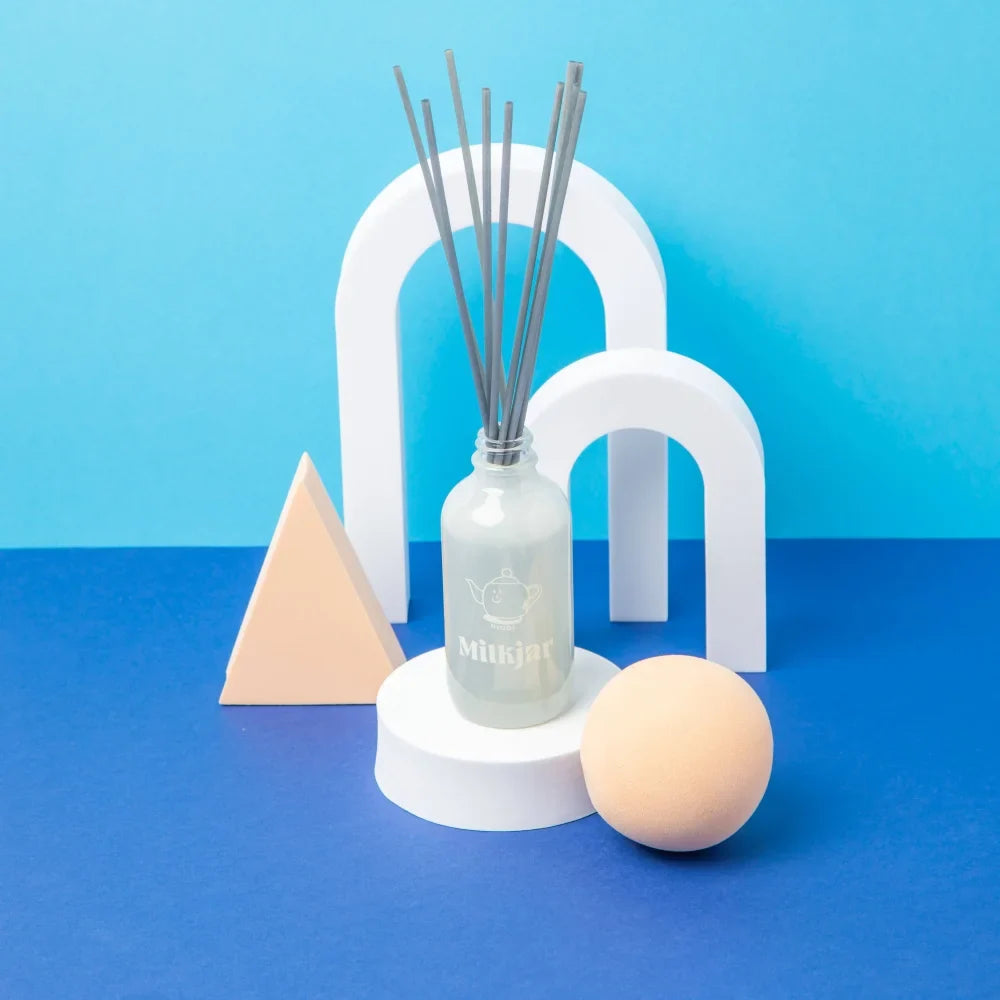 A frosted glass milkjar reed diffuser with gray reeds and teapot logo scented with vanilla tobacco and sea salt