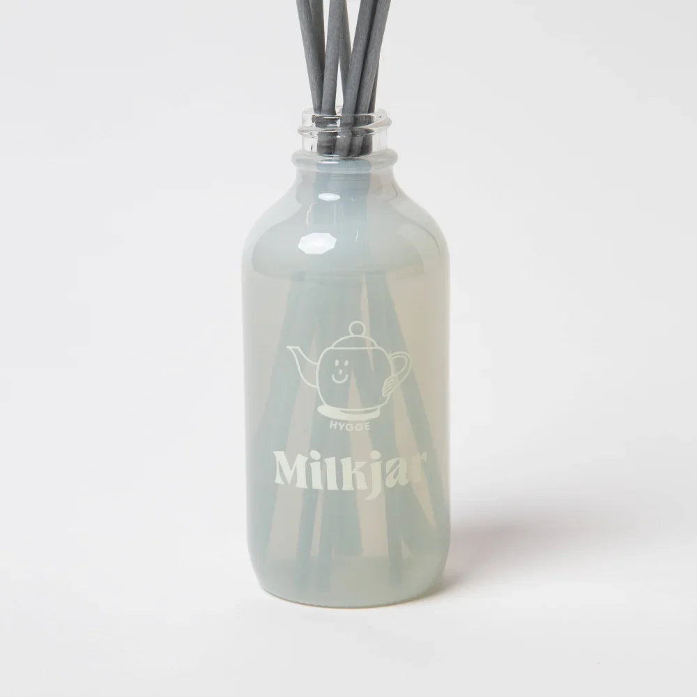 A frosted glass reed diffuser bottle with dark gray sticks and an etched teapot design labeled milkjar featuring sea salt scent