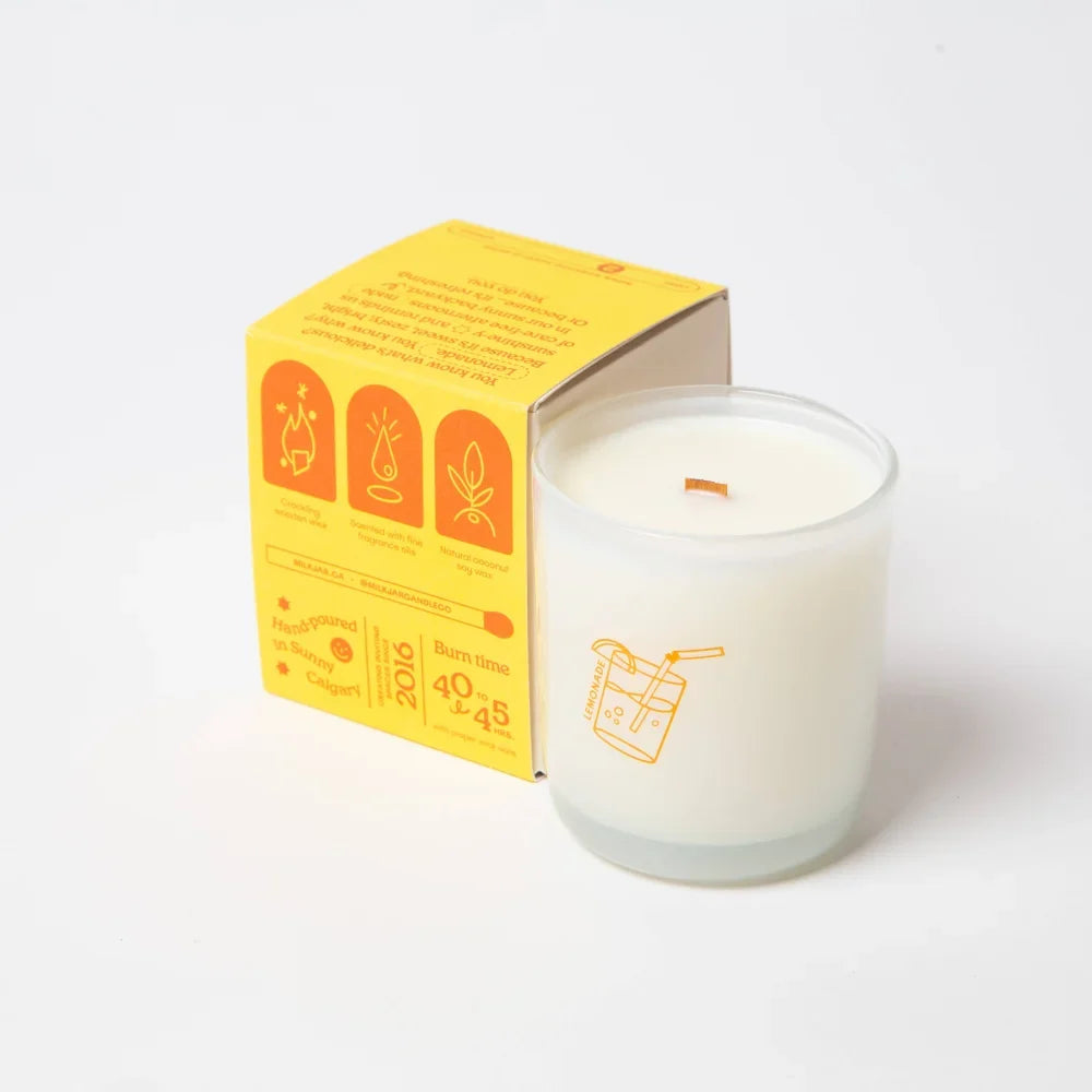 A white coconut soy candle in a clear jar with orange design, paired with its yellow lemonade coconut soy box