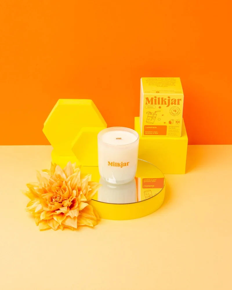 White milkjar candle in clear glass jar with orange branding lemonades coconut soy 8 oz candle