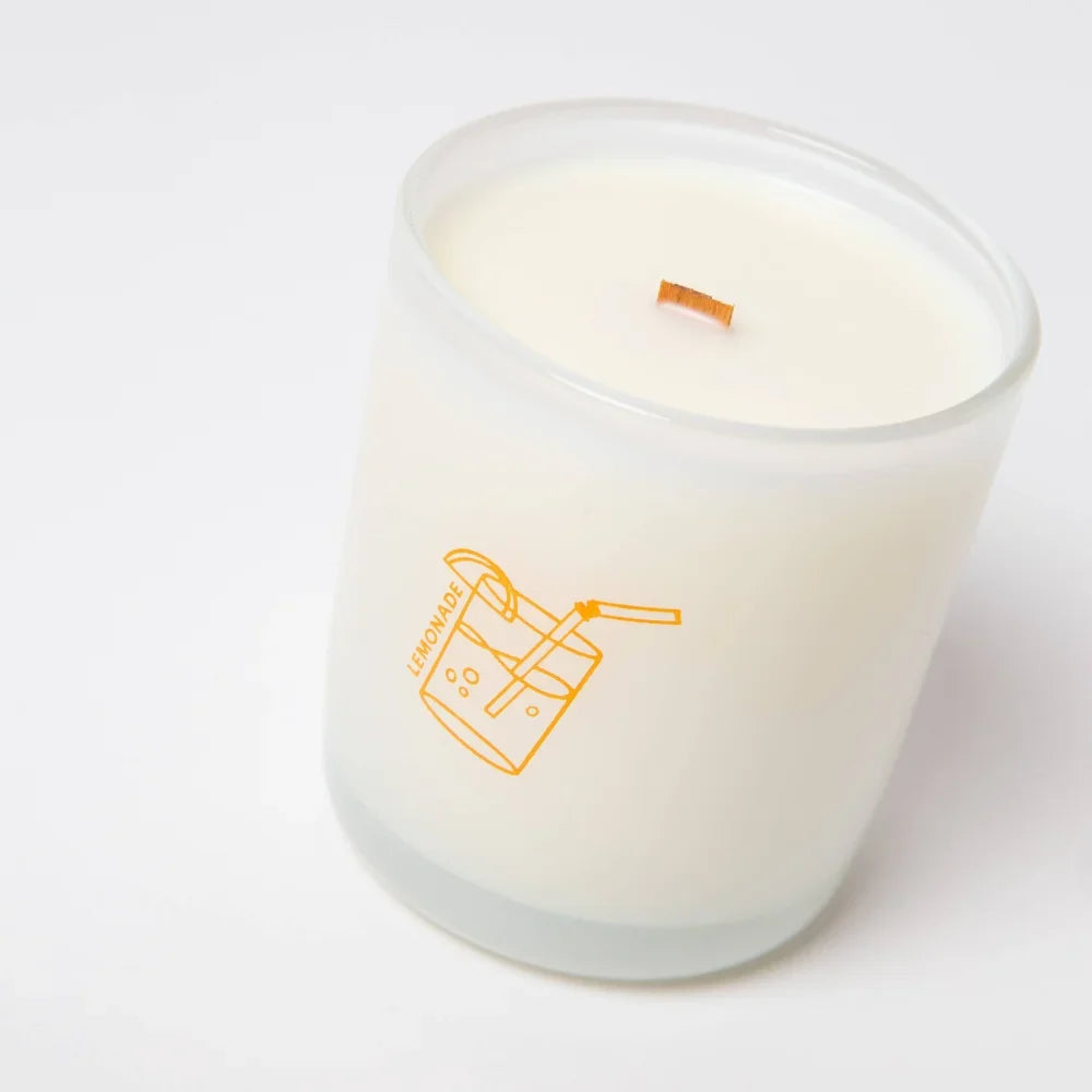 A creamy white lemonade scented coconut soy candle in a frosted jar with orange drink line art and lemonade text