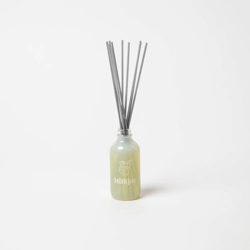 A sleek pale green glass reed diffuser with gray reeds for lemonade coconut lime verbena and pine scent