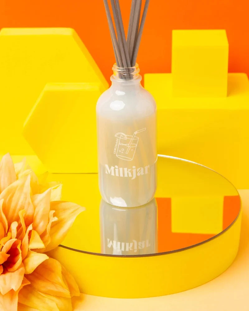 A frosted glass reed diffuser bottle with gray sticks and minimalist milkjar logo for lemonade coconut lime scent