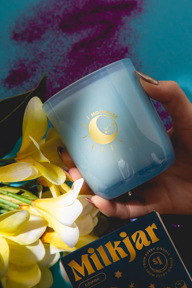 A translucent blue glass coconut soy candle with gold moon and sun design labeled i moonlit from moonrise neroli plum