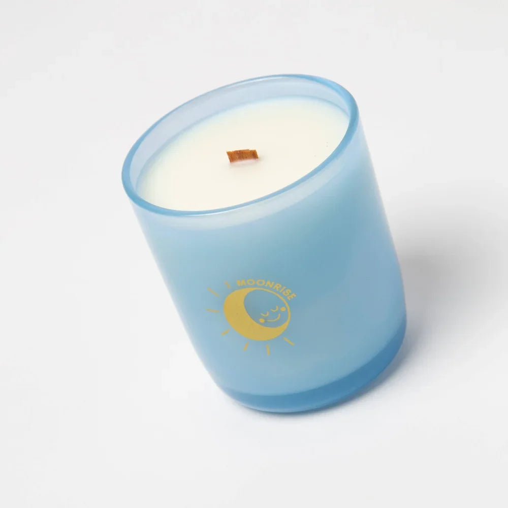 A light blue frosted glass coconut soy candle jar with gold moon and sun logo and creamy white wax wooden wick