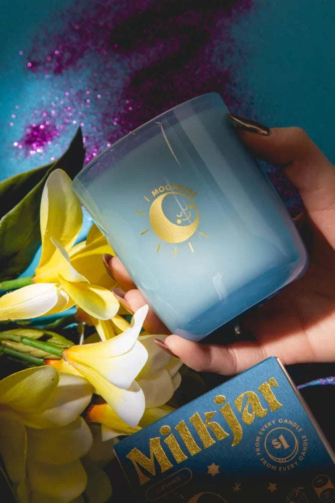 A translucent blue gradient coconut soy candle in a glass jar with gold moon and sun logo by milkjar labeled moonrise neroli plum