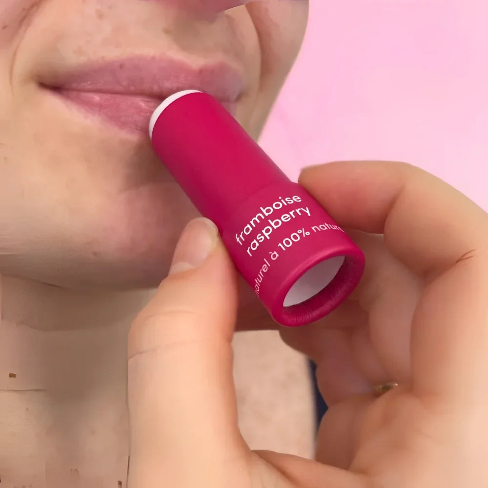 A vibrant pink raspberry natural lip balm tube held near lips showcasing 100 percent natural ingredients lip balms